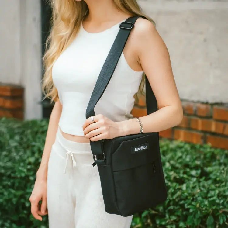 Person holding a black crossbody bag outdoors