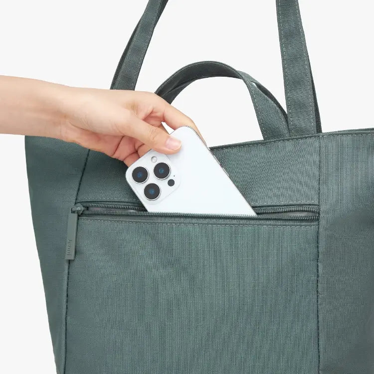 Person placing a white smartphone into a green tote bag.